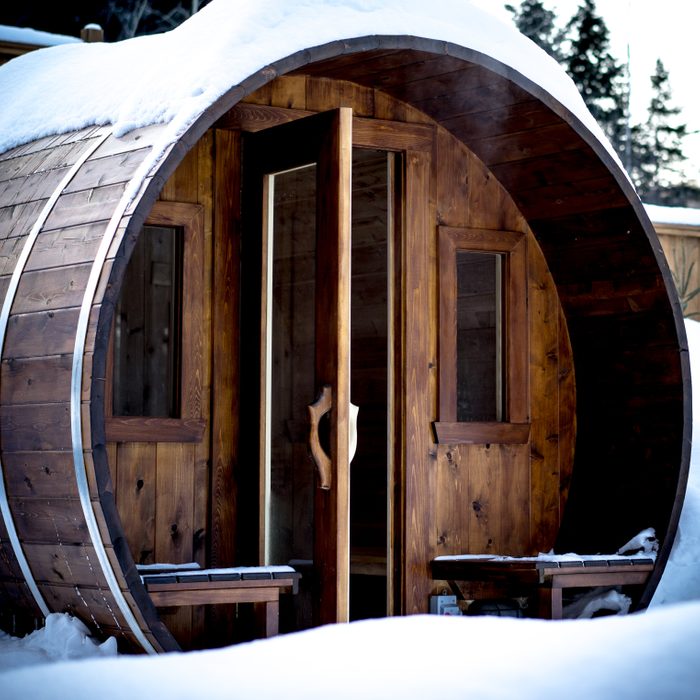 wooden outdoor sauna during a cold winter day with steam going out of the open door