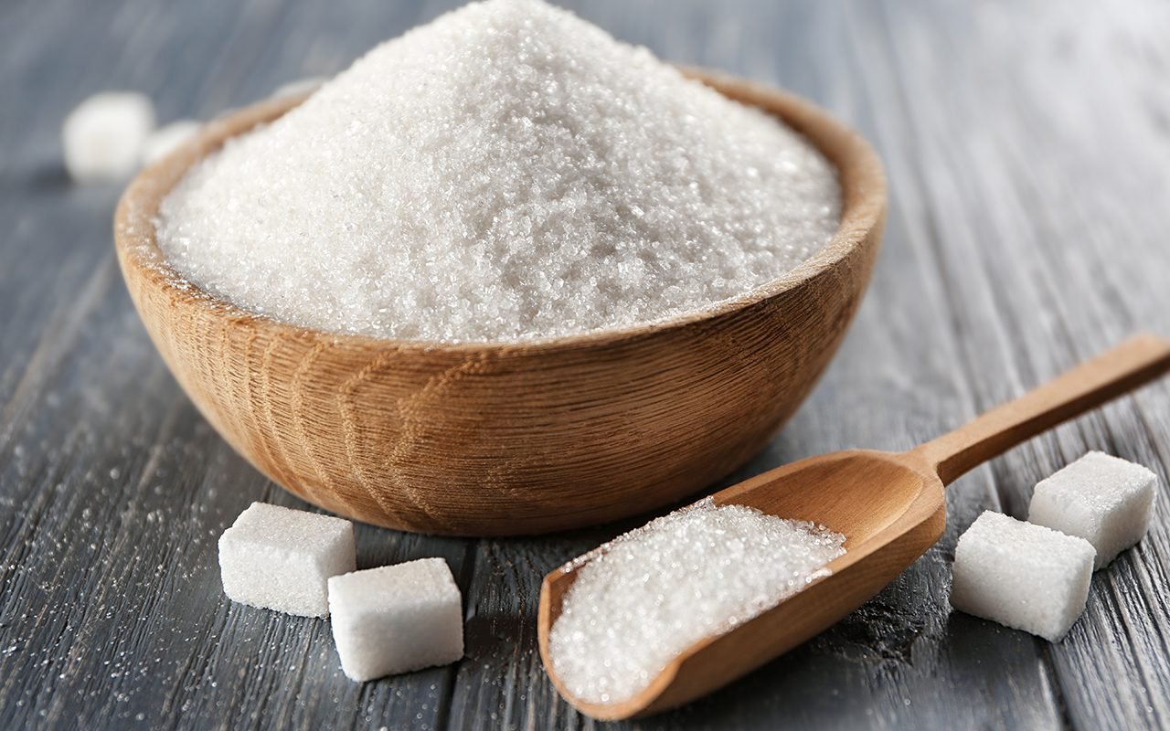 Bowl and scoop with white sand and lump sugar on wooden background