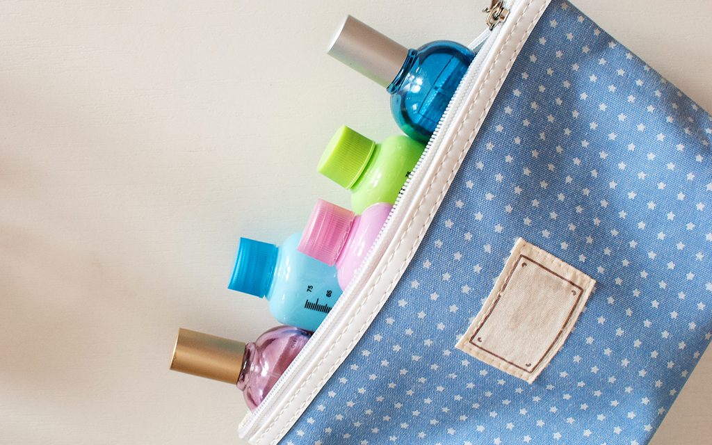 Blue travel toiletry bag with travel toiletries, small plastic bottles of hygiene products and perfume on white background.