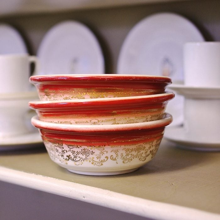 Vintage Stack of Bowls: close up of three orange & white bowls with a gold flowered pattern, stacked three high resting on a shelf amongst a backdrop of assorted white dishes at a thrift store.