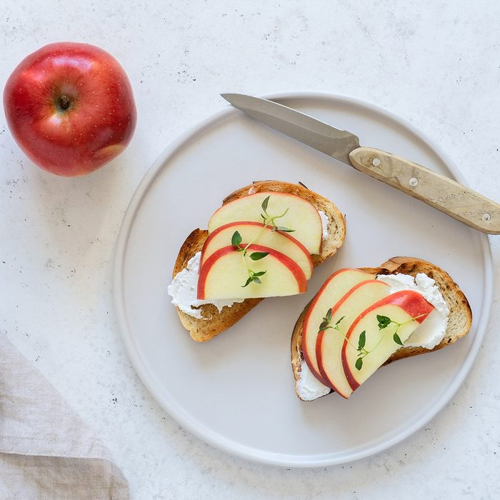 Toasts with apples, ricotta (cream cheese), thyme, served on white round plate. Summer breakfast. White stone background. Top view.; Shutterstock ID 1394007395; Job (TFH, TOH, RD, BNB, CWM, CM): TOH