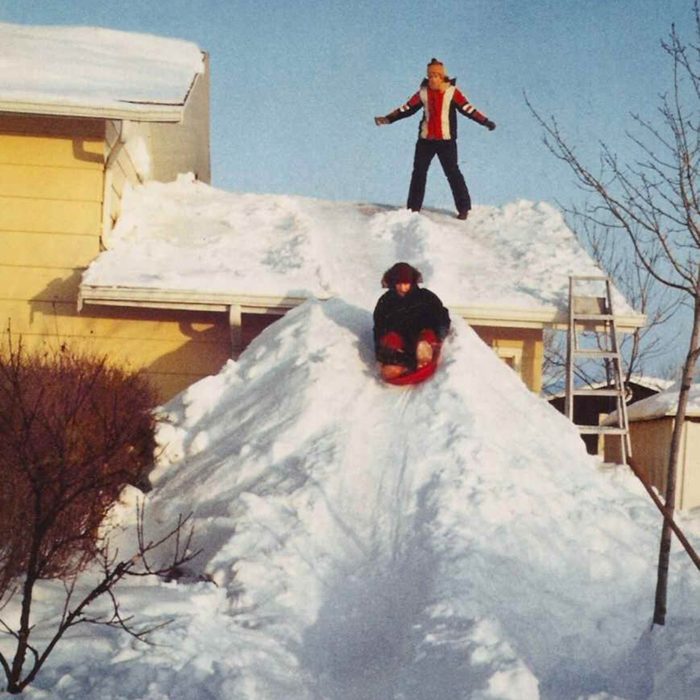 Kids sledding down a snow hill on the side of their house