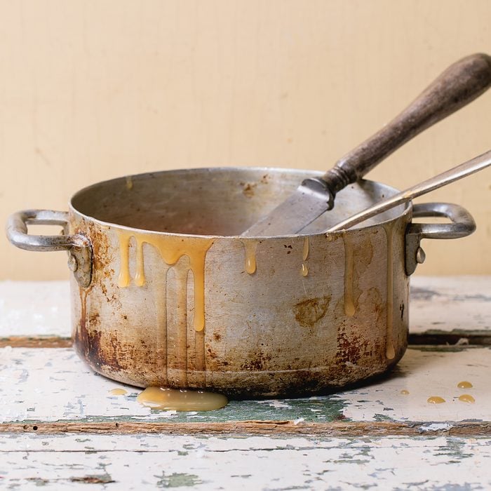 Old aluminum pan of homemade caramel sauce, served with spoons and sugar cubes over white wooden table. Selective focus, square image