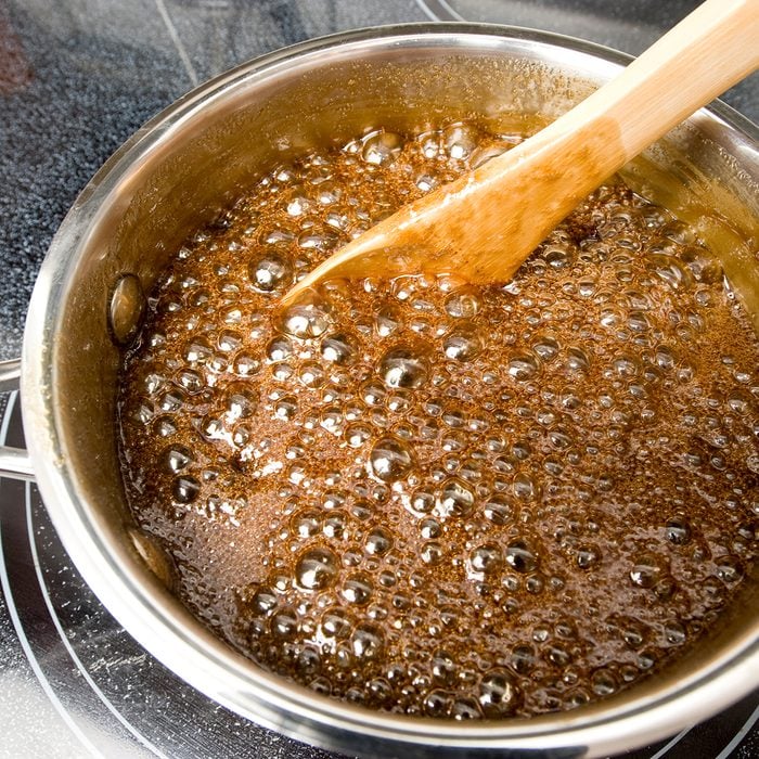 Home made caramel sauce cooking and bubbling on a stove top. Wood spoon. Stainless steel pot in a home kitchen