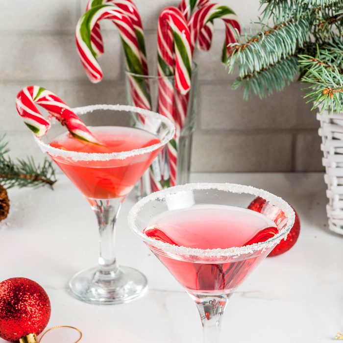 Christmas drinks, pink peppermint martini cocktail with xmas decoration and candy cane sweet on white marble kitchen table
