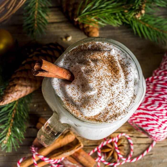 Christmas Tom and Jerry cocktail, whipped cream eggnog with spices, dairy milk beverage, with christmas decorations, rustic wooden background 