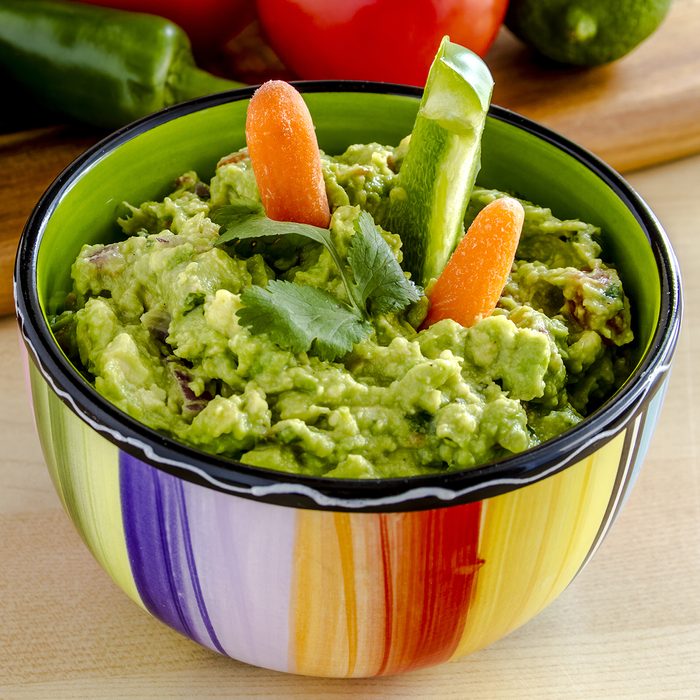 Fresh chunky guacamole in colorful bowl garnished with raw carrots and green peppers and cilantro