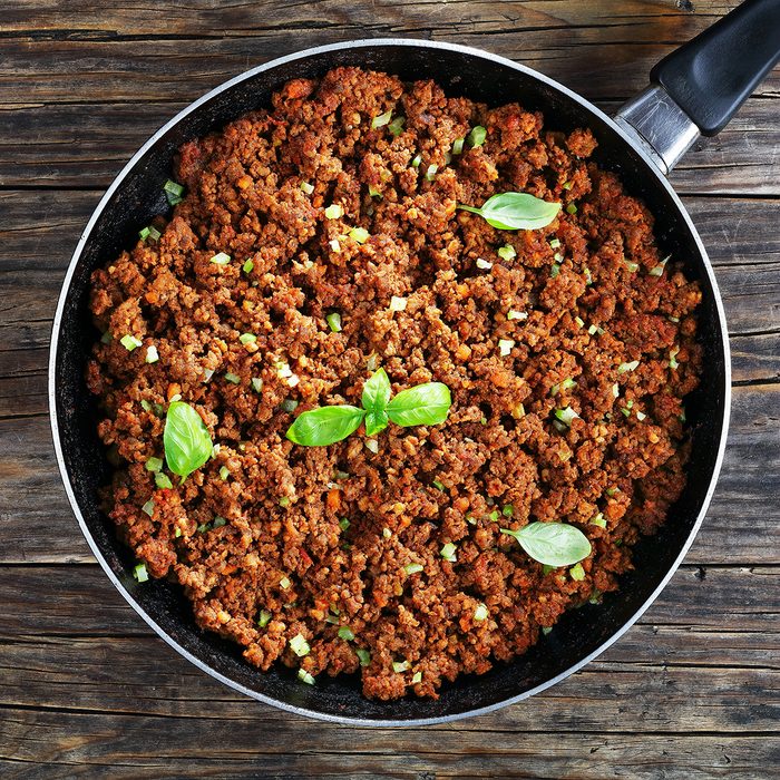 bolognese sauce - hot juicy ground beef stewed with tomato sauce, spices, basil, finely chopped vegetables and celery in skillet on wooden table