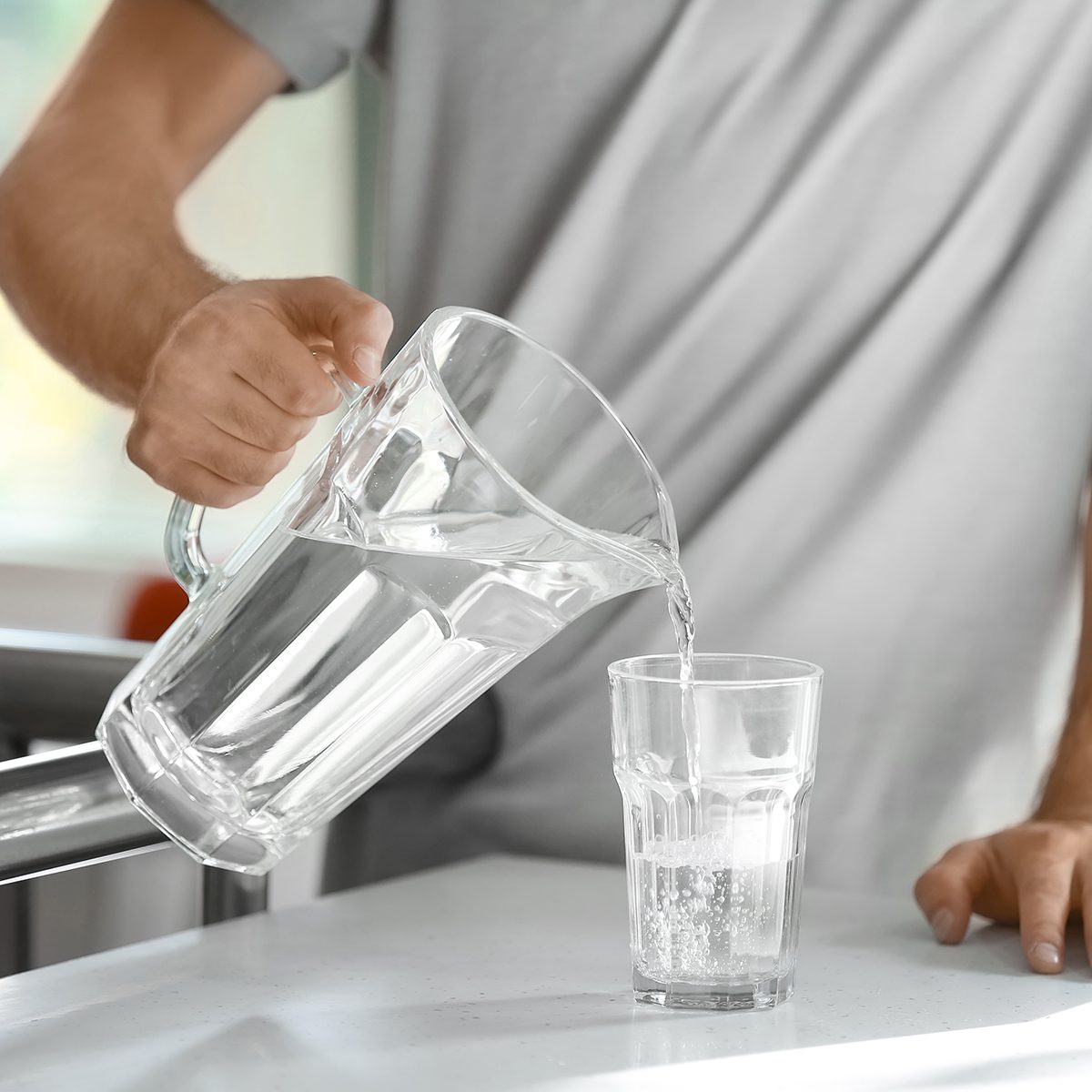 Morning of young man pouring water into glass in kitchen
