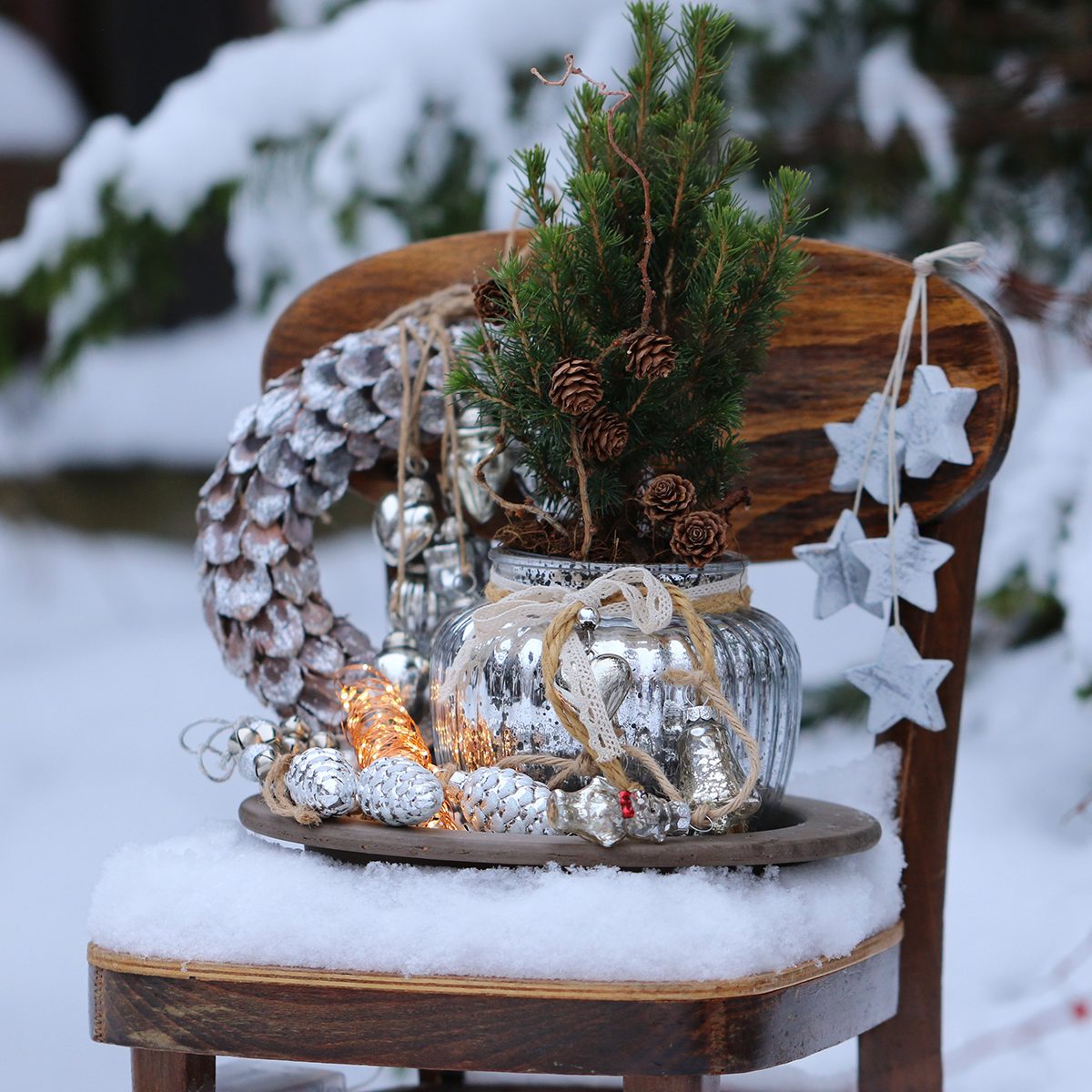 Winter composition with Christmas wreath, glass decoration, garland, fir tree, wooden star on vintage wooden child chair on snow, natural background, outdoor and space, scene in snow garden