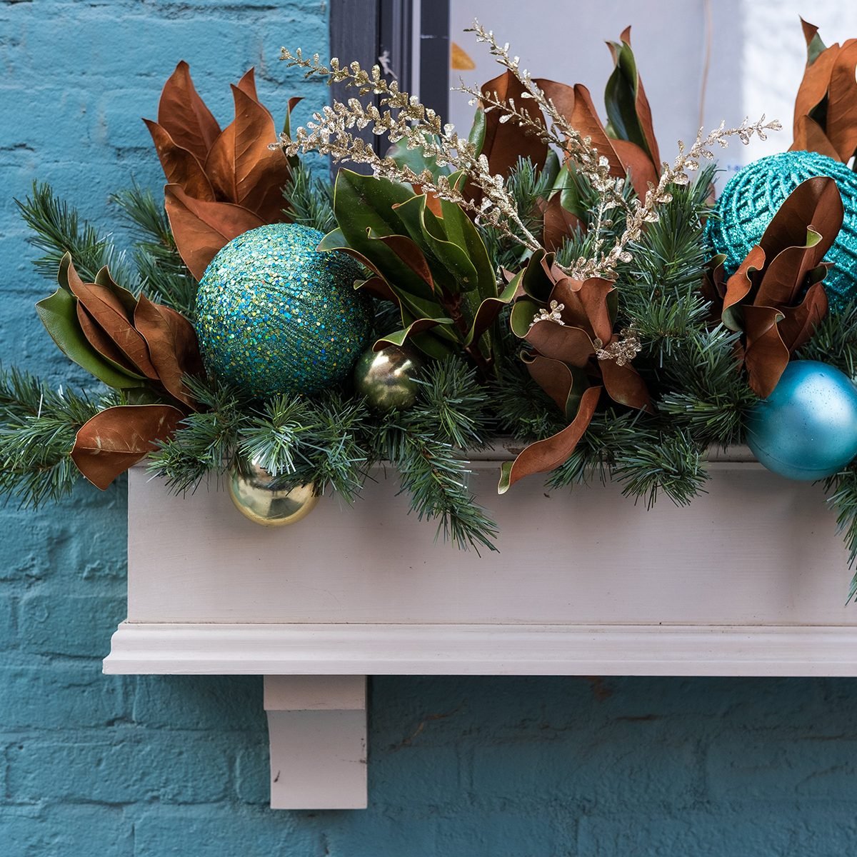 A close-up of the left side of a window planter box decorated for Christmas, set against a bright blue brick building.