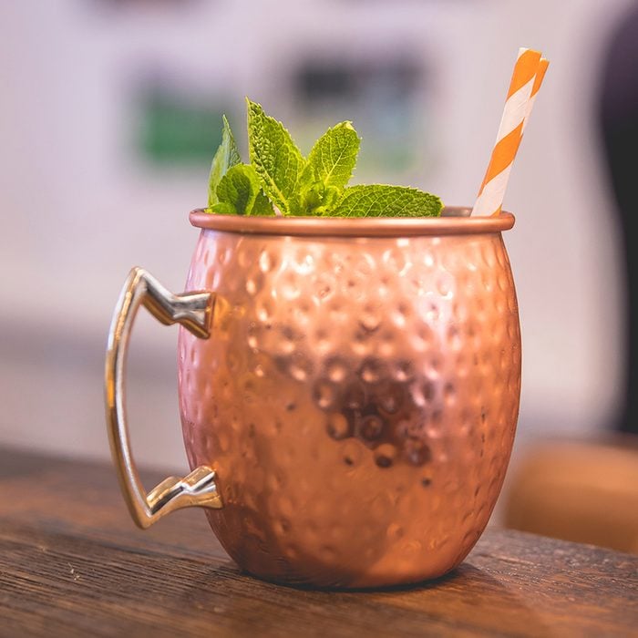 Close up on a copper cup with Moscow Mule cocktail, fresh mint as decoration and a white and orange carton straw; Shutterstock ID 1165209037; Job (TFH, TOH, RD, BNB, CWM, CM): TOH