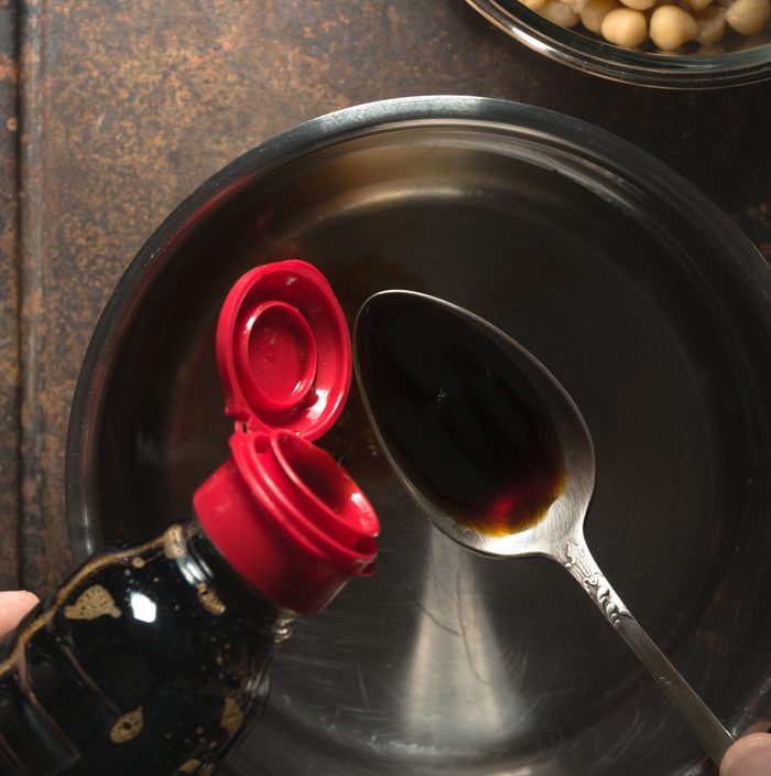 Soy sauce is poured into a spoon over the saucepan