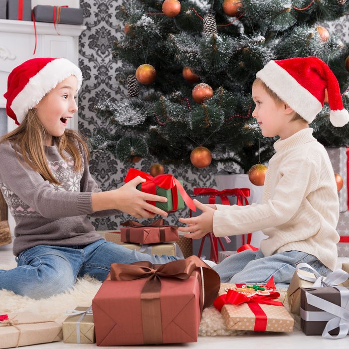 Cute happy excited children, boy and girl in santa hats unwrap christmas present.