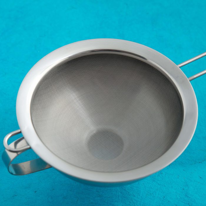 Stainless steel funnel with sieve insert. Blue kitchen background.