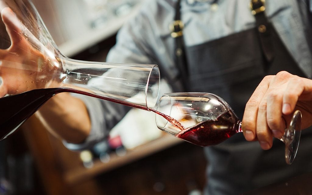 Sommelier pouring wine into glass from mixing bowl.