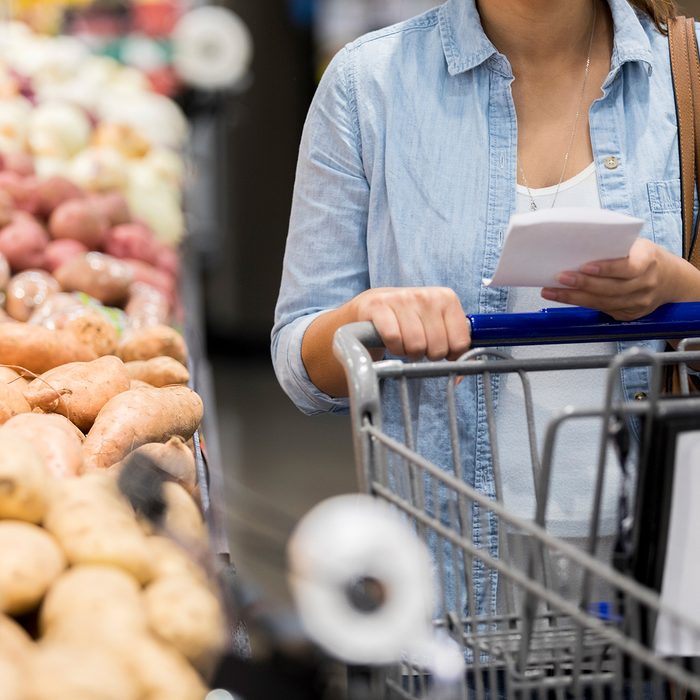 Person in a grocery store pushing a cart while reading their list