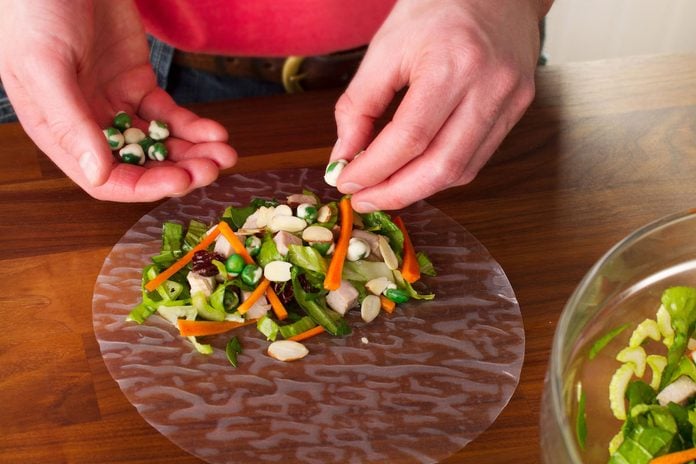 A person filling a spring roll wrapper with fresh vegetables.