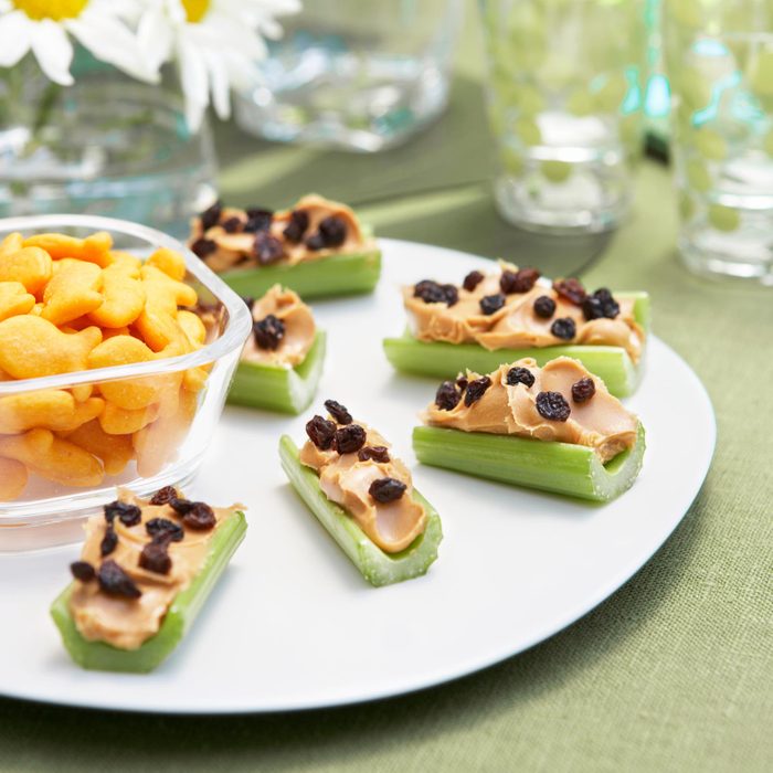 a plate with celery topped with peanut butter and raisins with a bowl of gold fish crackers to the side