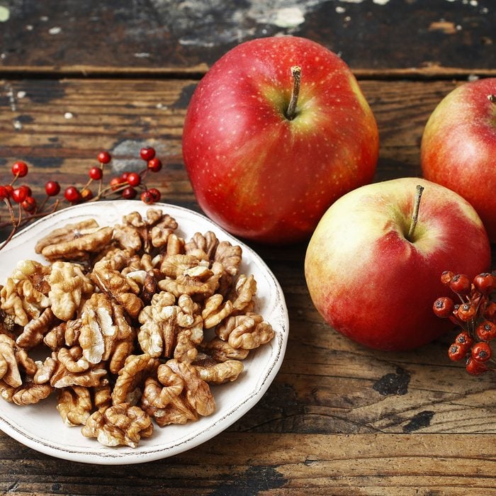 Bowl of walnuts and red apples on wooden table. Healthy snacks.