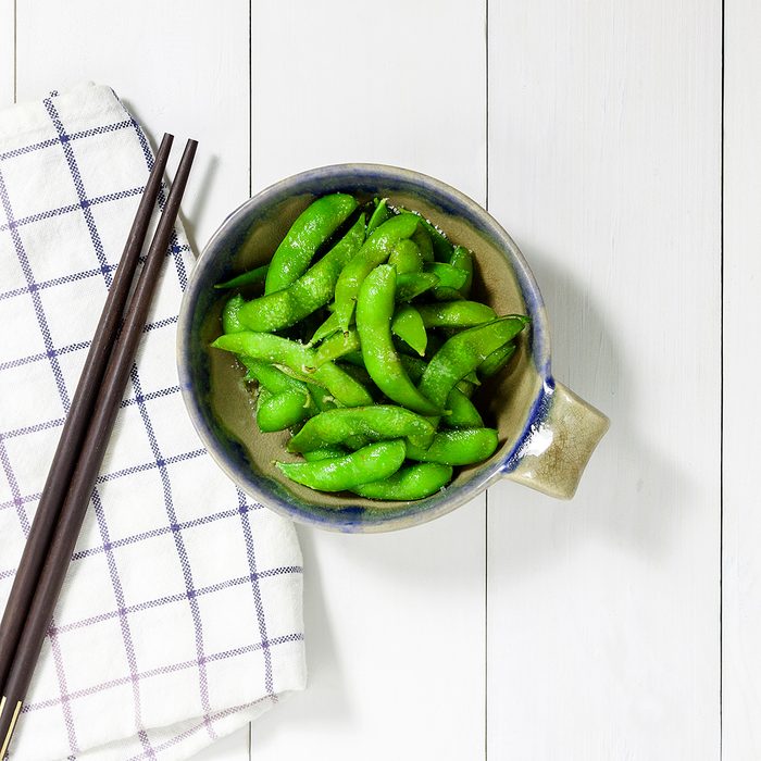 edamame nibbles, boiled green soy beans, japanese food, Top view on white wooden table