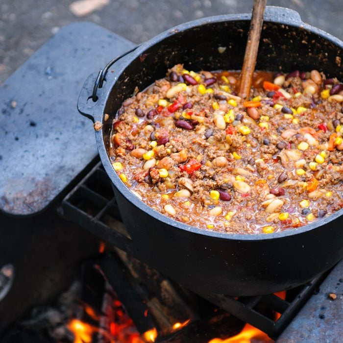 Large cast iron pot of spicy chili cooking over a campfire