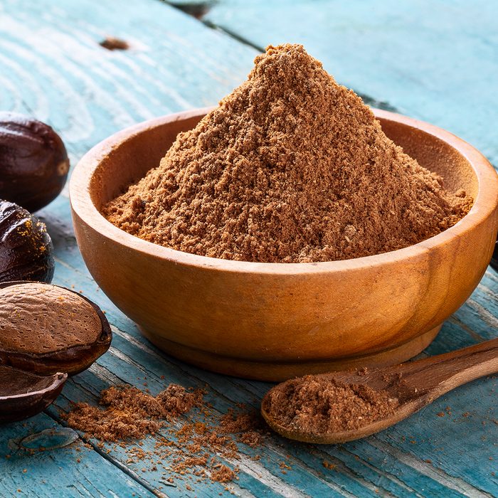 Whole inshell nut, cracked and nutmeg powder in a wooden bowl and spoon on old blue rustic background close-up. indian spice.