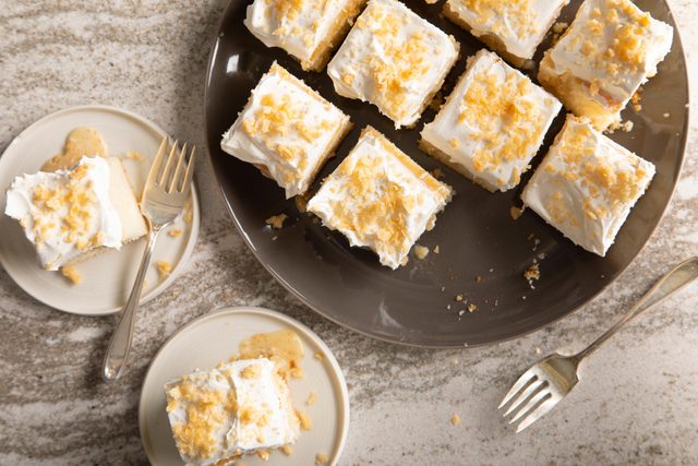 Oklahoma Coconut Poke Cake With Toasted Shredded Coconut sliced up on a serving dish and on two plates