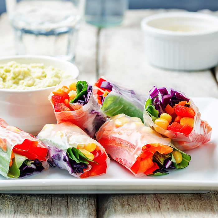 rainbow spring rolls with avocado white bean hummus on white wood background.