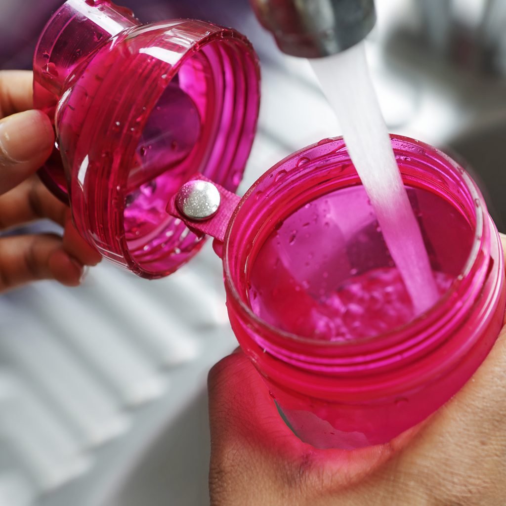 The tap is running with water into the pink water bottle