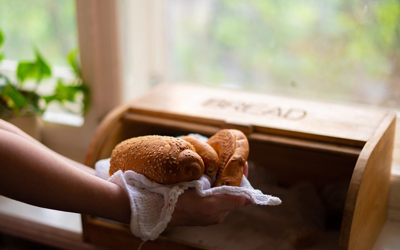 woman taking a bread loaf from a bread box in the kitchen at home