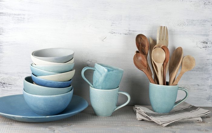 Simple rustic handmade blue crockery against white wooden wall: dish, stack of bowls. mugs and wooden cooking utensils set.