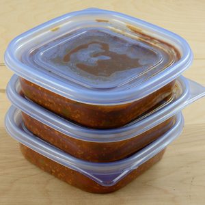 Batch of freshly made spaghetti sauce with ground turkey meat in plastic storage containers to prepare for freezer and meals in advance for work week
