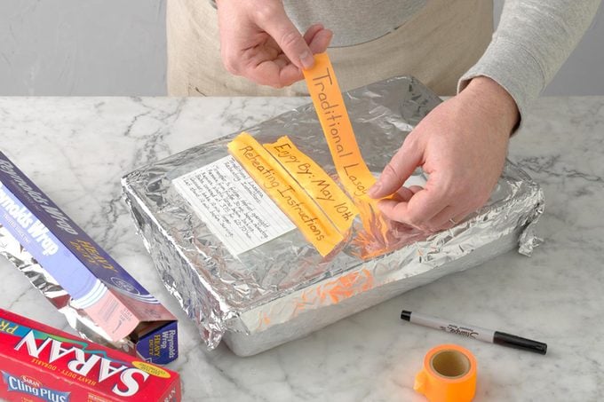 frozen lasagna; marble surface; how to; plastic wrap; foil, marker; colored washi tape; hands