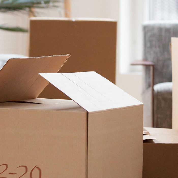 Close up carton boxes with belongings man sitting on sofa hold phone on background, wait call to delivery service moving at new house concept, banner for website header design with copy space for text