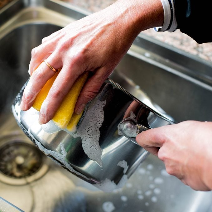 Woman Washing Up a Stainless Steel Saucepan in the Kitchen Sink After Cooking