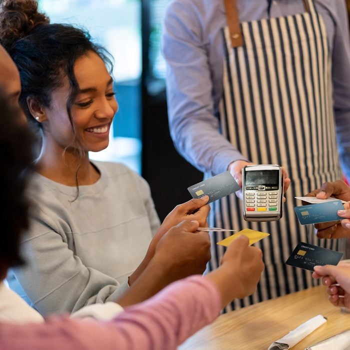 Happy group of friends paying with a credit card at a restaurant and splitting the bill â business concepts. **DESIGN ON CARDS WERE MADE FROM SCRATCH BY US**
