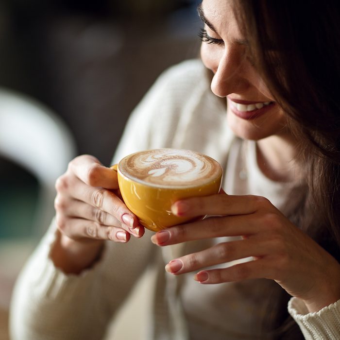 Young smiling woman holding cup of latte coffee.