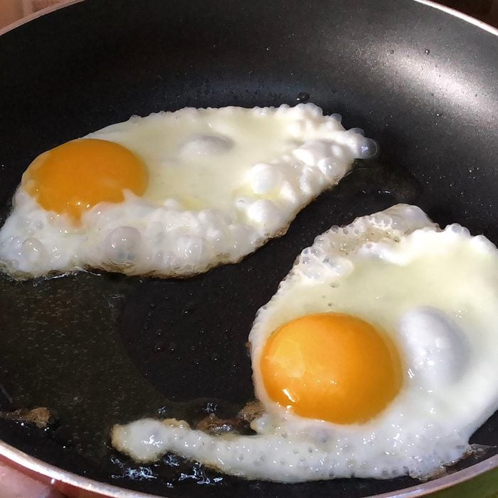 Photo showing two fried eggs that are being cooked in a greasy frying pan, as part of a full-English fried breakfast fry-up.