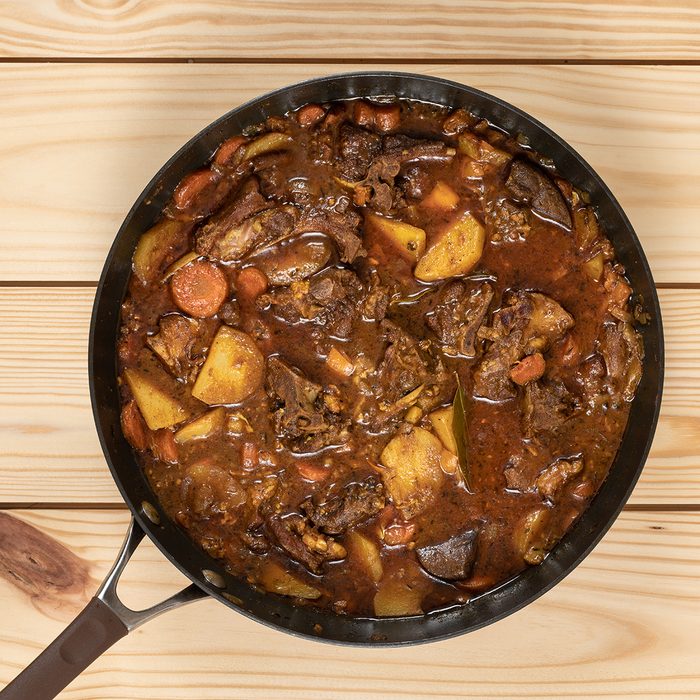 Close-up of colorful goat stew in cooking pan on top of wooden table.