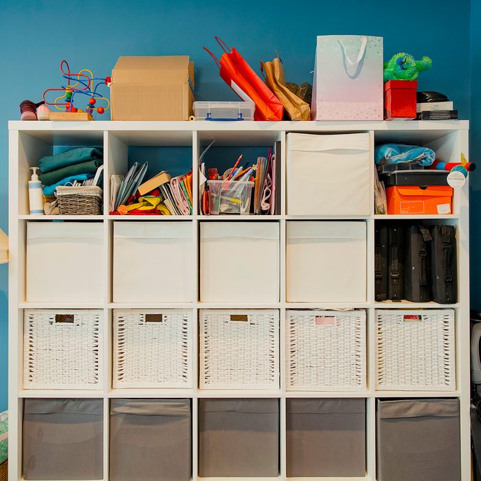 Front view of a storgae unit in a home. The storage unit has many draws and compartments for storage. Some household objects have been stored on top of the unit.