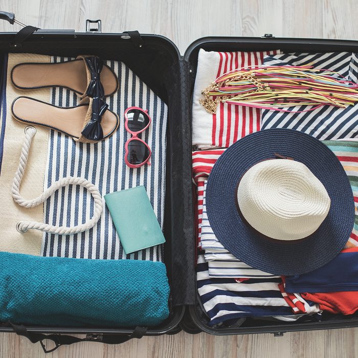 High angle view of summer clothes, slippers, sun hat, sun glasses, beach towel, and other accessories arranged in a suitcase.