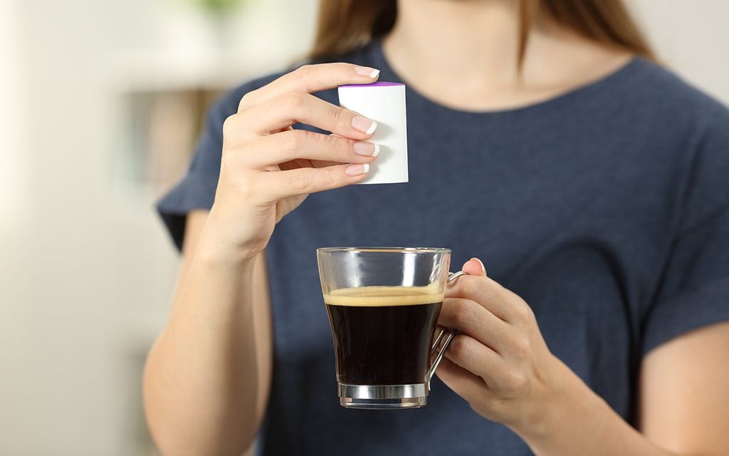 Front view close up of a woman hands throwing saccharin into a coffee cup at home