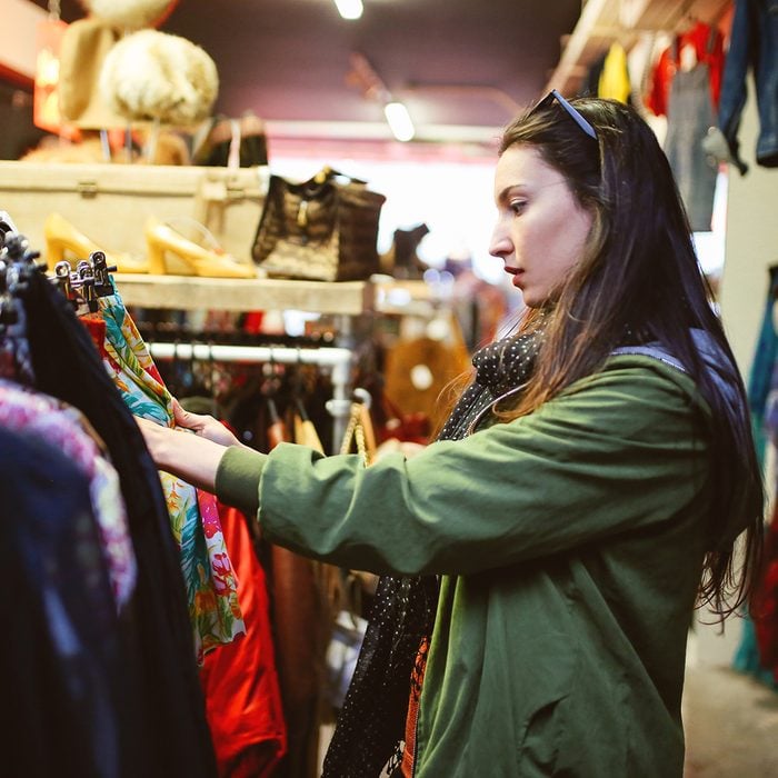 Vintage toned portrait of a young beautiful brunette woman in London second hand marketplace. She is wearing casual Autumn clothes, an olive green parka jacket, browsing through the stuff in the market.