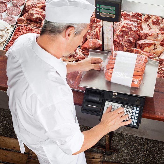 High angle view of male butcher weighing sausages at display cabinet in butchery; Shutterstock ID 242663593