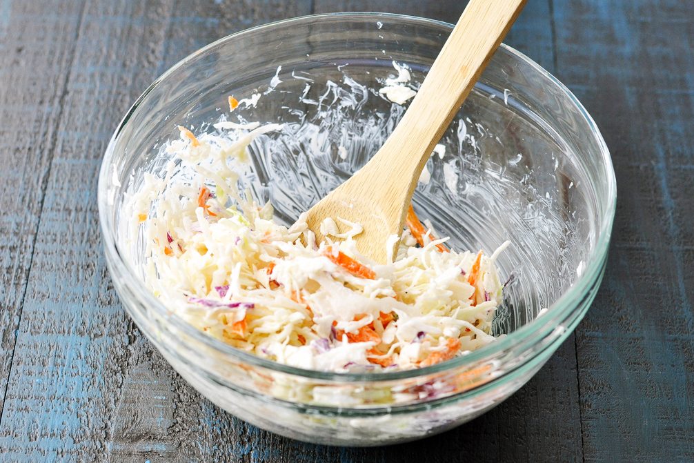 a wooden spoon in a glass bowl mixing coleslaw