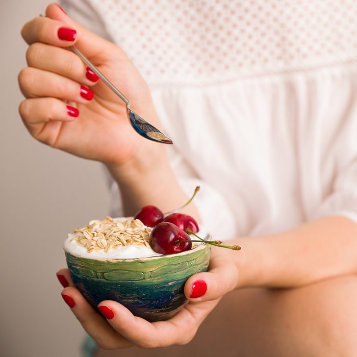 Closeup of woman's hands holding a cup with organic yogurt with oats and cherries. Homemade vanilla yogurt in girl's hands. Breakfast or snack. Healthy eating and lifestyle concept.