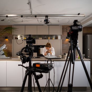 food vlogger v-logger blogger influencer woman recording video vlog vlogging in tv-show studio kitchen for social media behind the scenes film and audio equipment visible