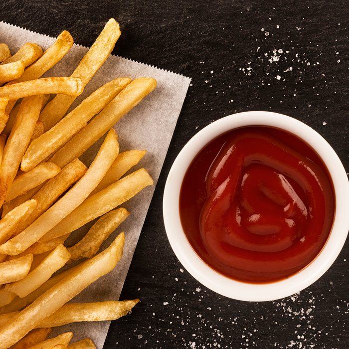 French fries with ketchup on dark background, directly above. Close up.