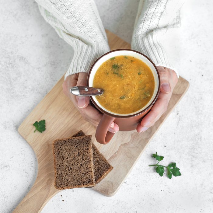 Woman hands holding mug of vegetable soup on white background - healthy winter vegetarian food, cozy warming soup.
